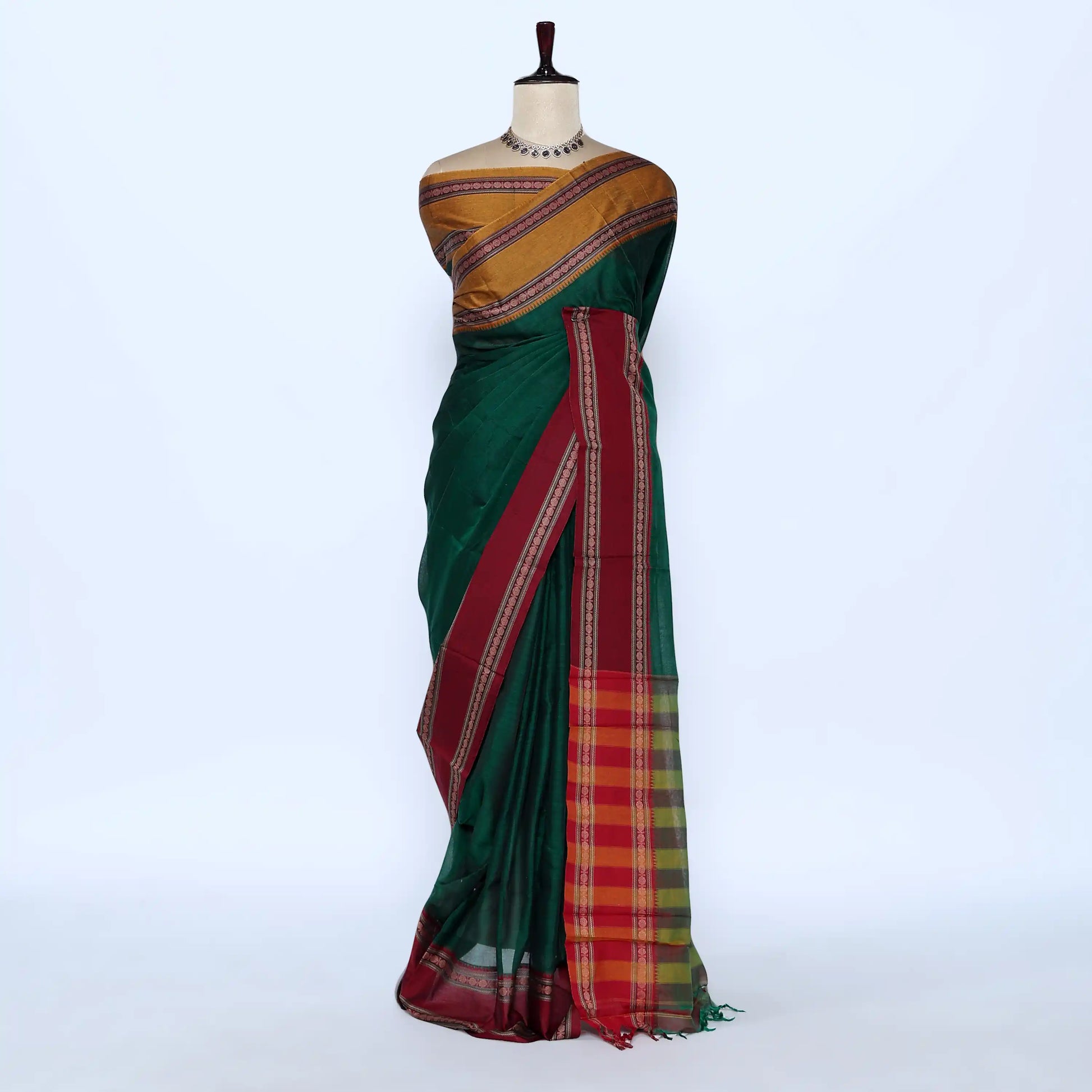A dark green silk saree with a gold and red patterned blouse and a red border