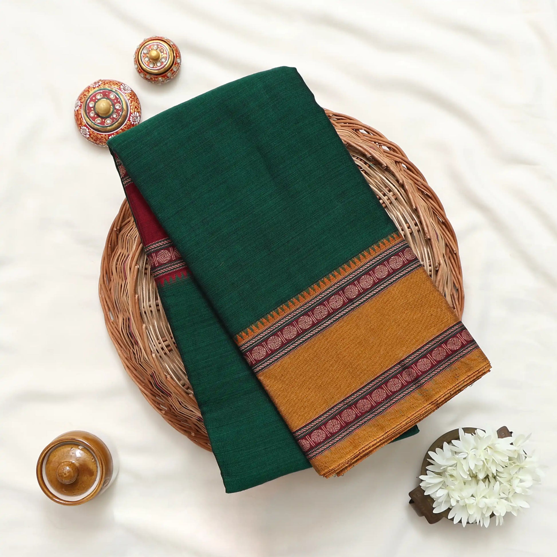 A folded dark green saree or fabric piece with a wide mustard-gold border and red patterned stripes