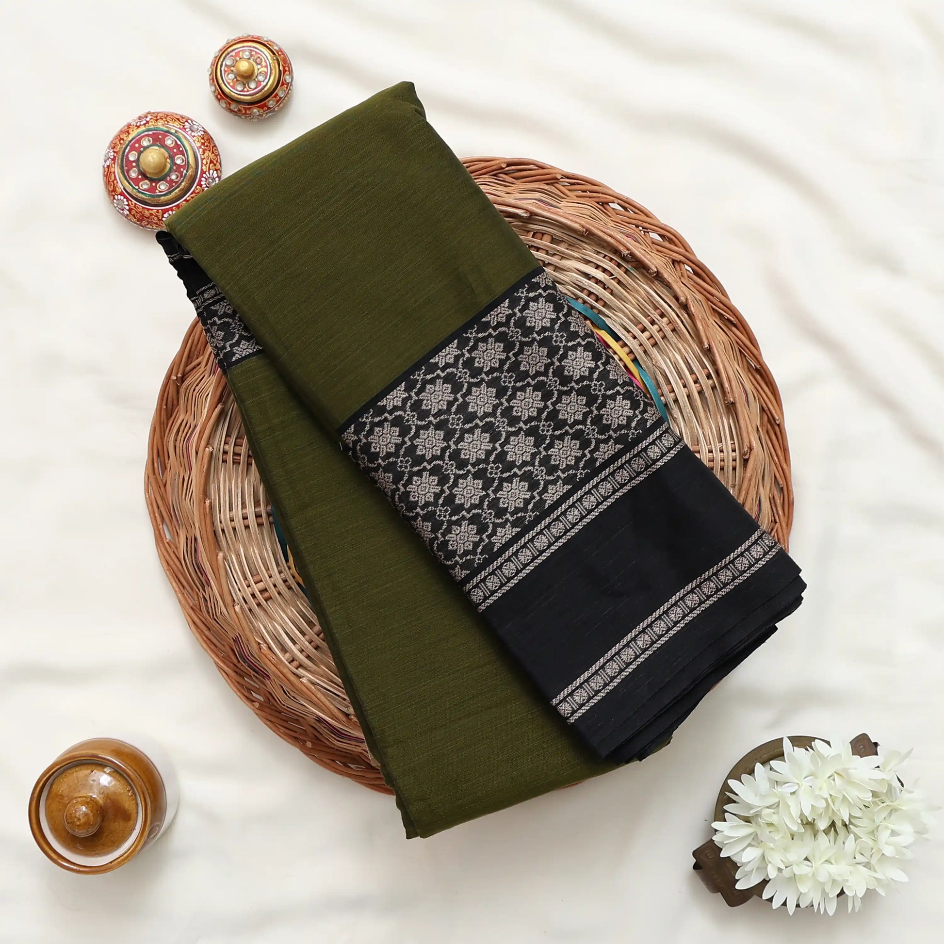 A folded dark green and black fabric garment, likely a sari or scarf, featuring a detailed black and gray floral border