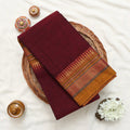 A folded deep maroon saree with a wide golden and red patterned border