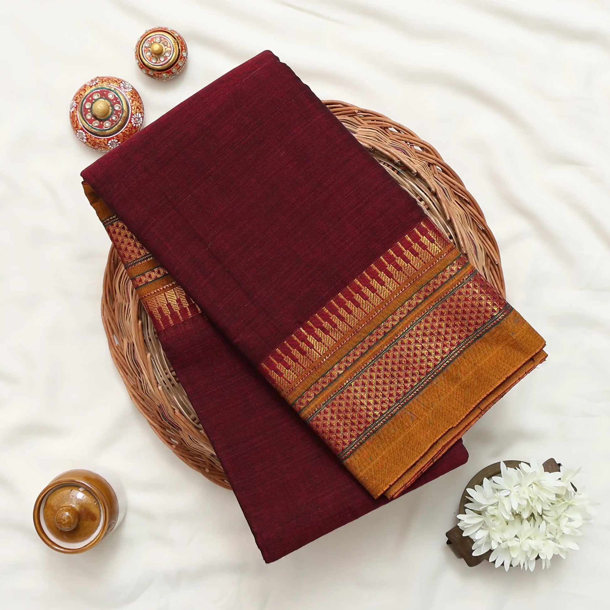 A folded deep maroon saree with a wide golden and red patterned border