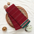 A folded deep red saree  with white stripe details and a green patterned border