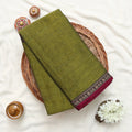 Narayanpet cotton saree with plain olive green body and paisley zari woven border folded top view on wicker basket.
