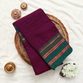 Top view of purple Narayanpet cotton saree with green zari woven border neatly folded on a wicker basket display.