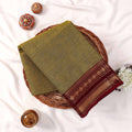 Kanchi Cotton Saree With Maroon And Gold Zari Border In Olive Green Color Folded Flat Lay View With Decor
