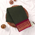 Kanchi Cotton Saree With Gold Zari Border In Dark Olive Green And Magenta Folded Flat Lay View On Wicker Tray
