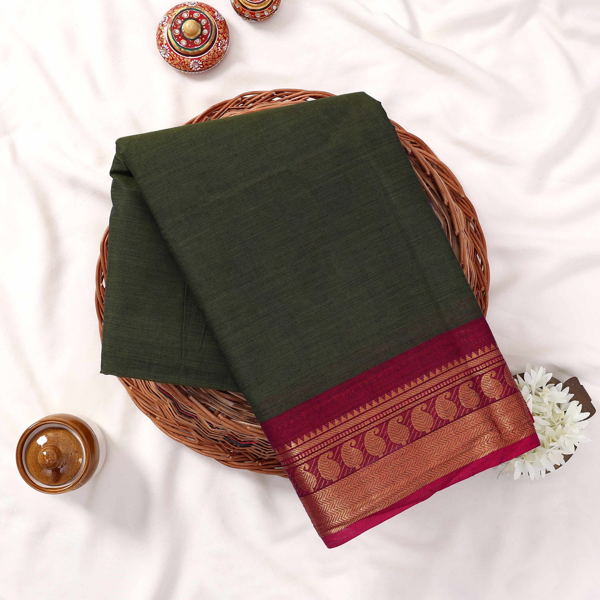Kanchi Cotton Saree With Gold Zari Border In Dark Olive Green And Magenta Folded Flat Lay View On Wicker Tray
