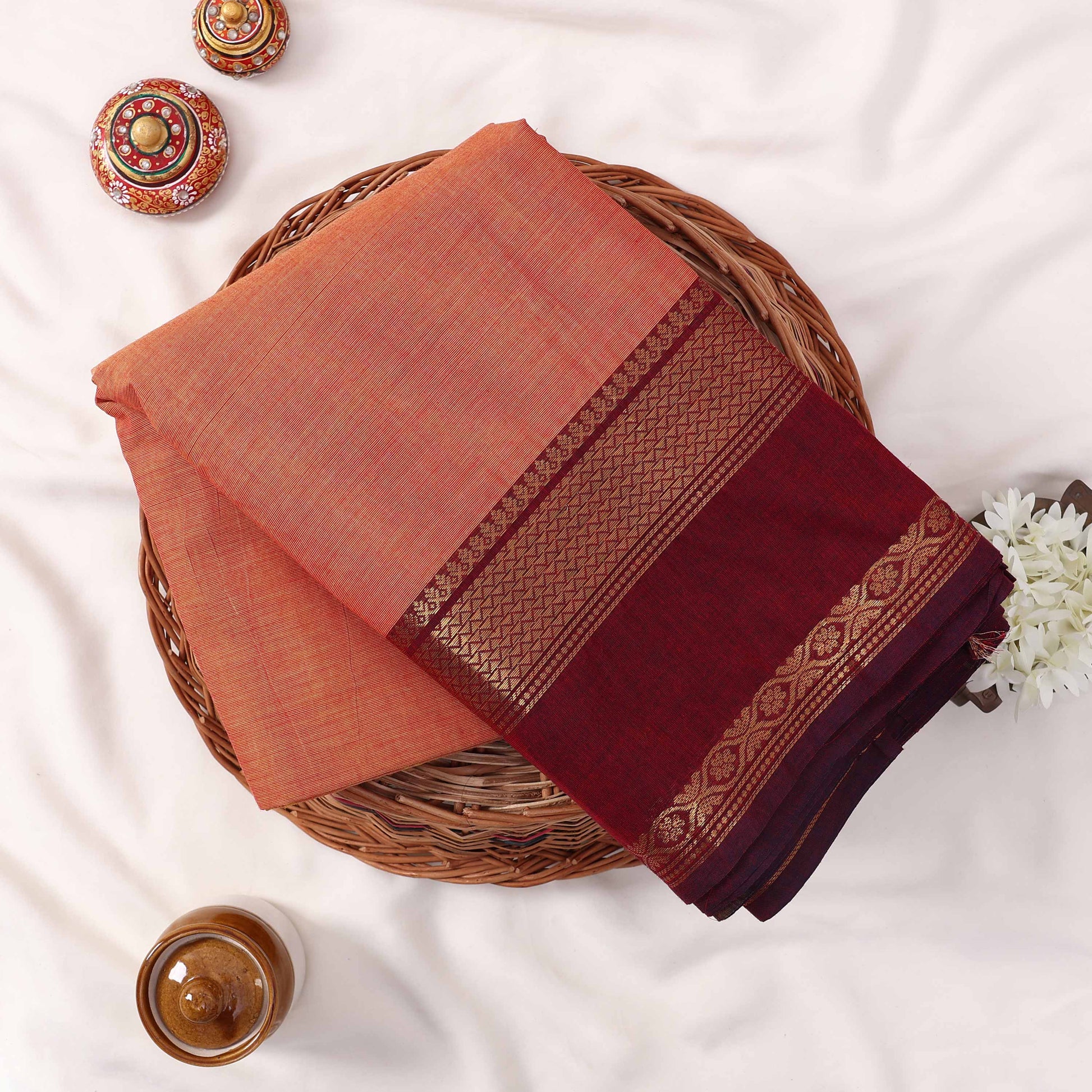 Kanchi Cotton Saree With Orange Body And Maroon Zari Border Folded Display Showcasing Woven Detailing Top View With Decorative Styling
