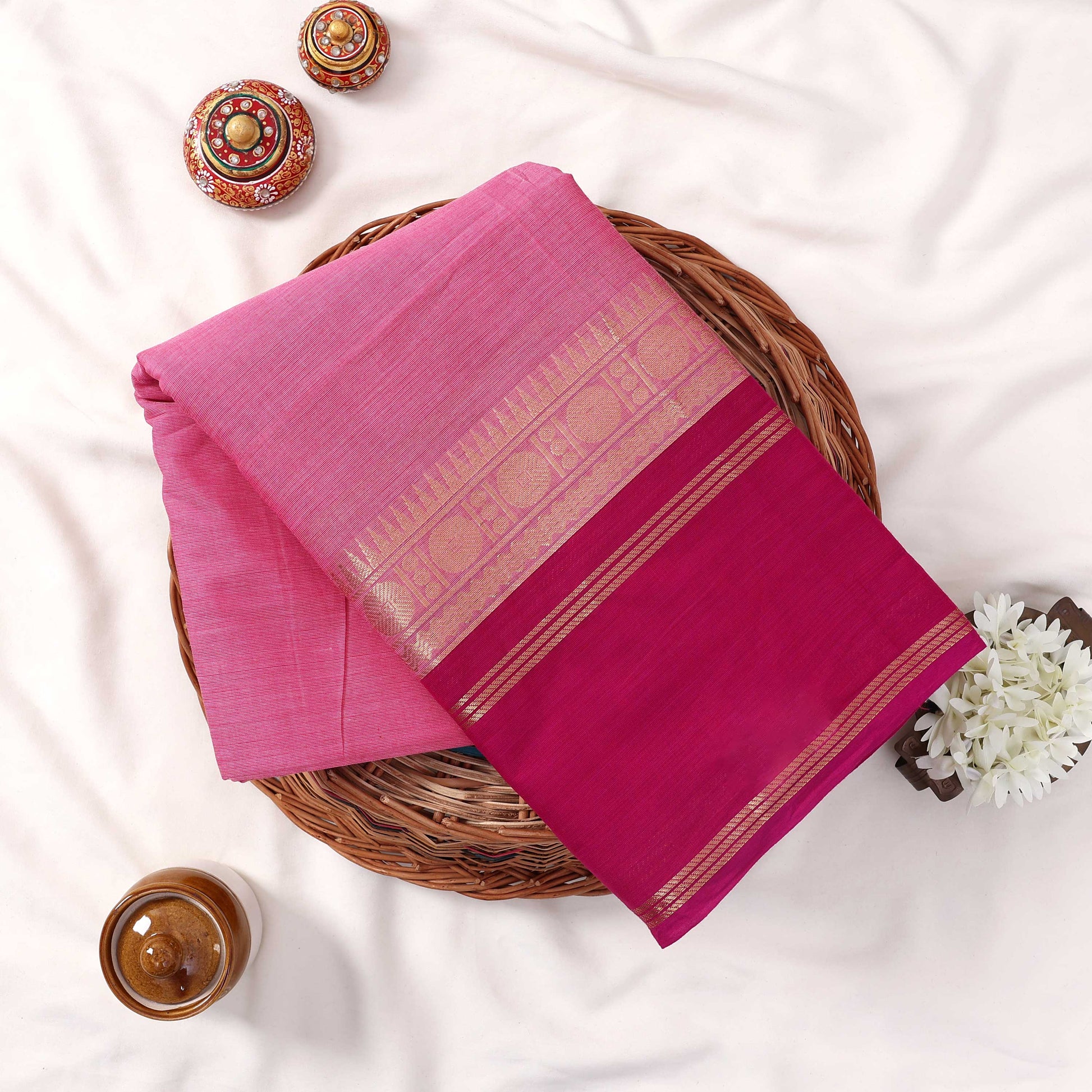 Kanchi Cotton Saree With Light Pink Body Magenta Zari Border And Woven Texture Folded Top View On Wicker Tray
