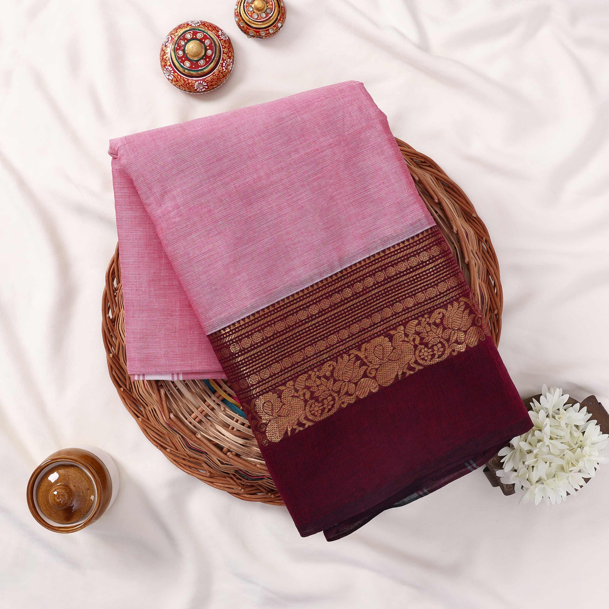 Kanchi Cotton Saree With Floral Zari Border In Pink And Maroon Folded Flat Lay View With Decorative Accents
