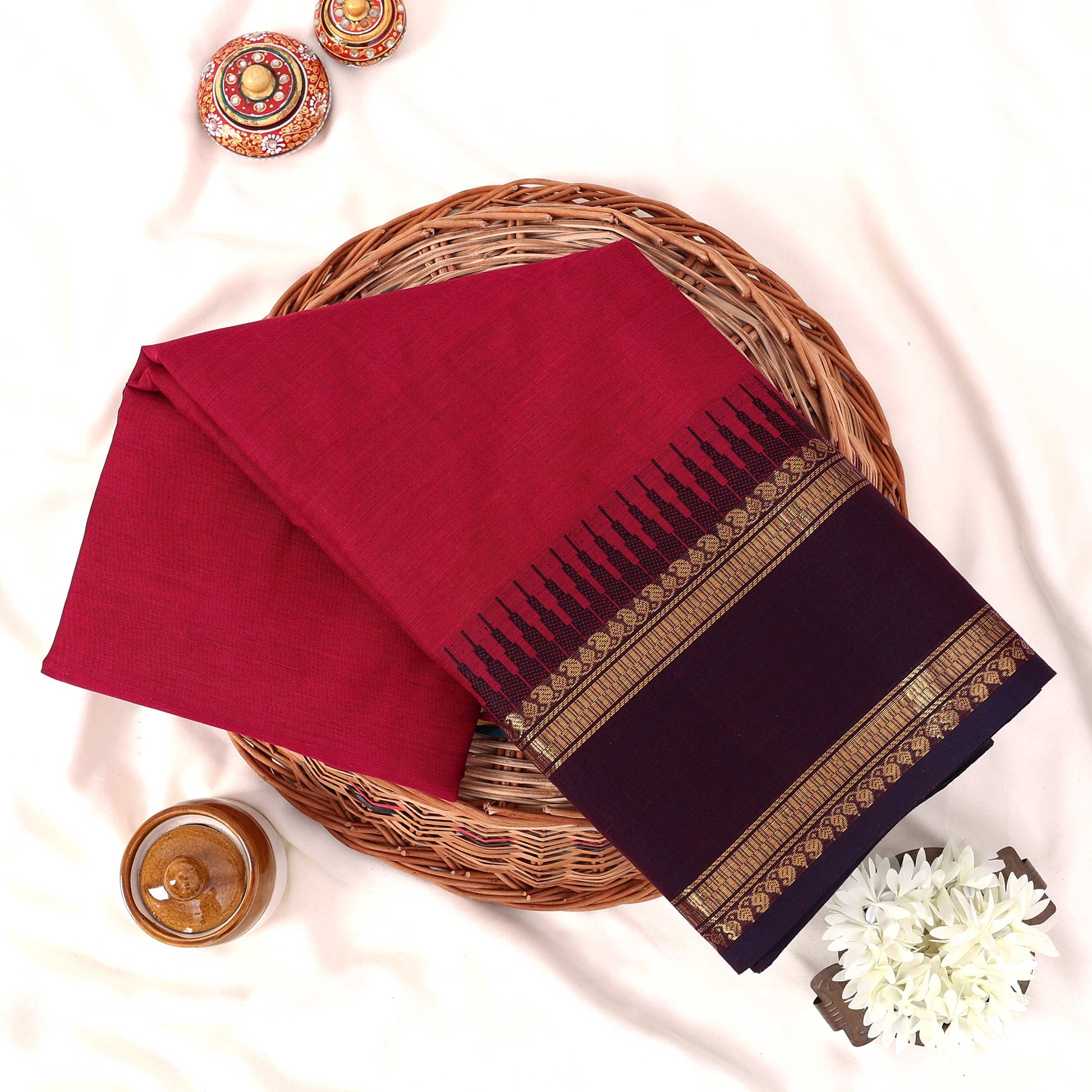 Kanchi Cotton Saree With Gold Zari Border In Deep Pink And Purple Folded On Basket Top View Display

