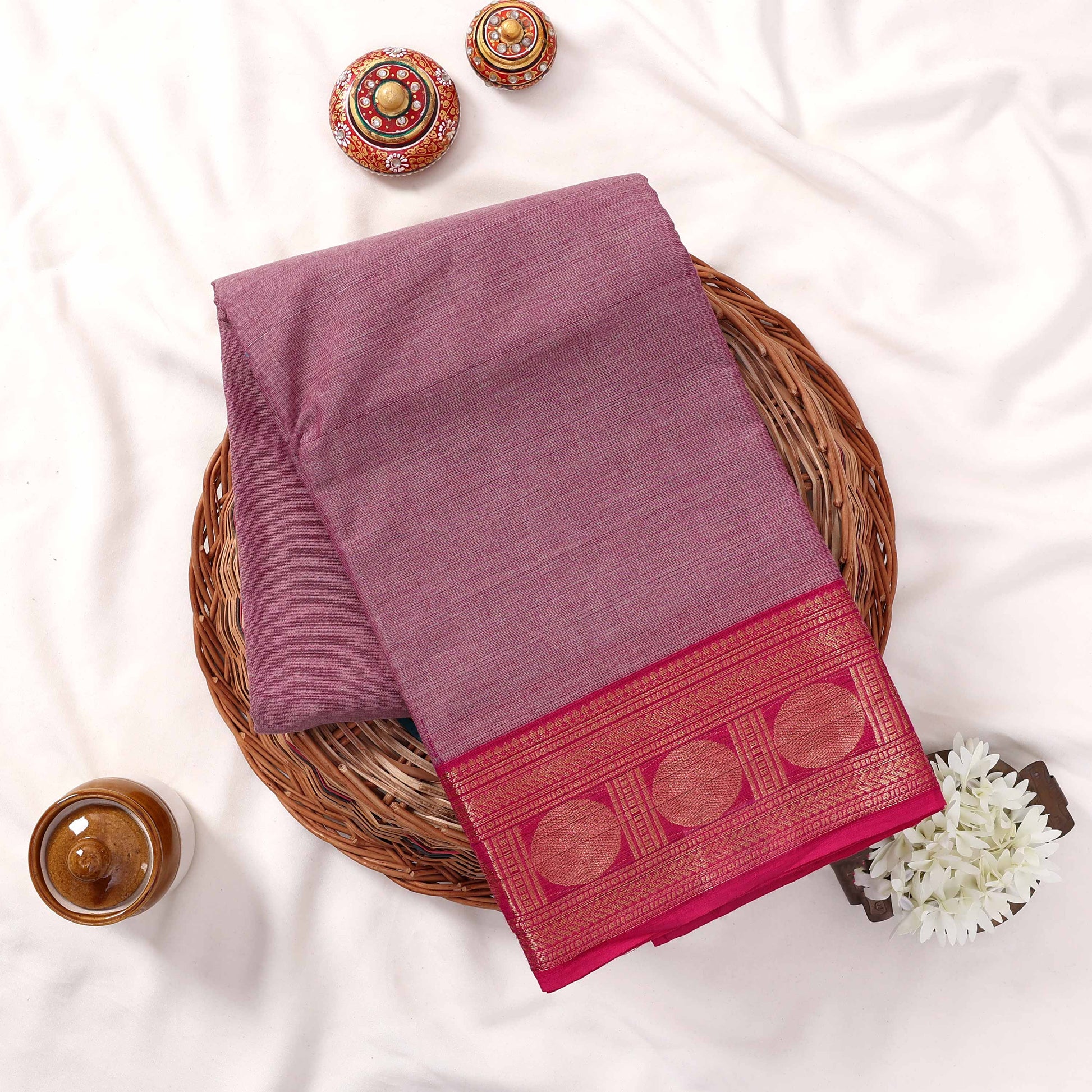 Kanchi Cotton Saree With Zari Border In Deep Purple And Maroon Folded On A Wicker Basket Top View Display
