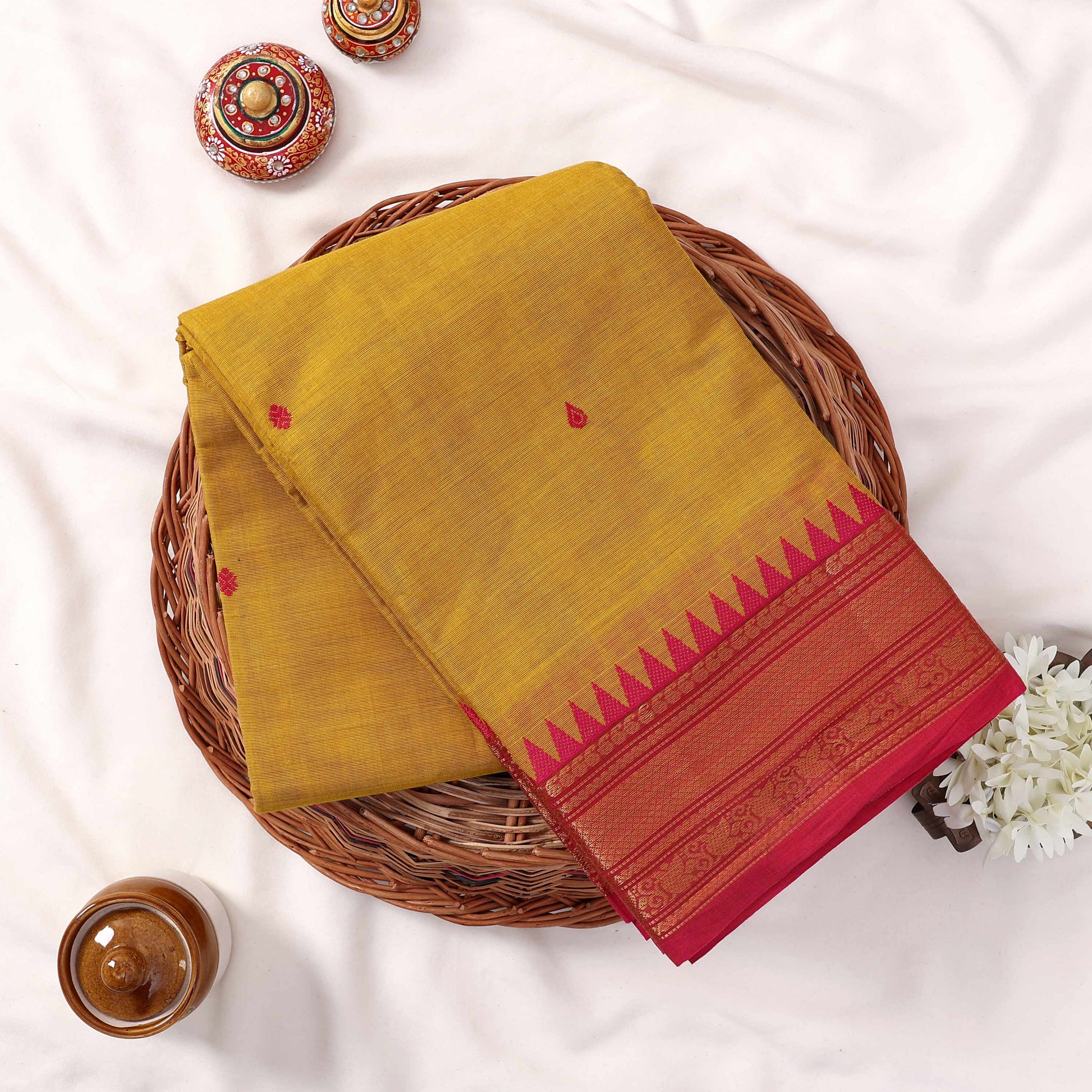 Kanchi Cotton Saree With Yellow Weave Pink Zari Border And Butta Motifs Top View Folded Display On Wicker Tray
