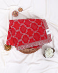 A folded red fabric item with a white geometric bandhani-style pattern and a decorative embroidered border