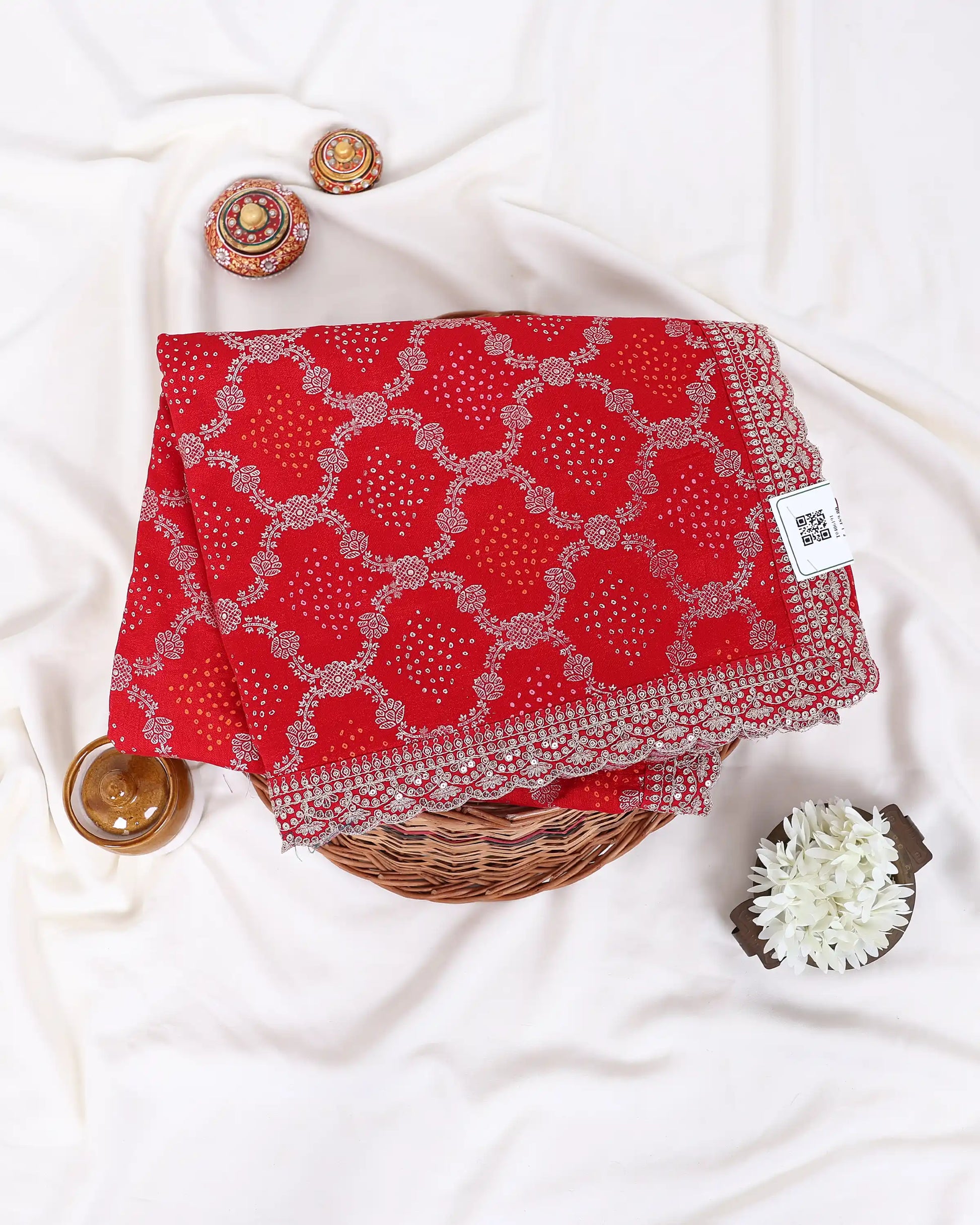 A folded red fabric item with a white geometric bandhani-style pattern and a decorative embroidered border