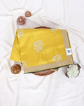 A folded yellow saree with white floral motifs and a gold border