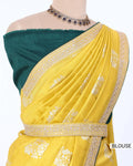 A yellow Banarasi silk saree with white floral motifs and gold zari borders, paired with a dark teal green blouse