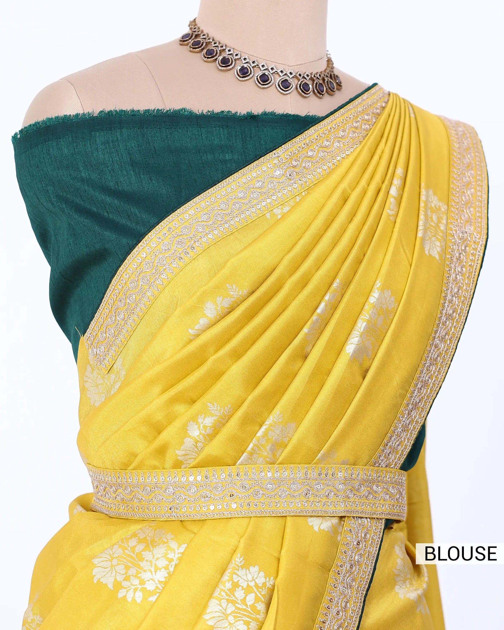 A yellow Banarasi silk saree with white floral motifs and gold zari borders, paired with a dark teal green blouse