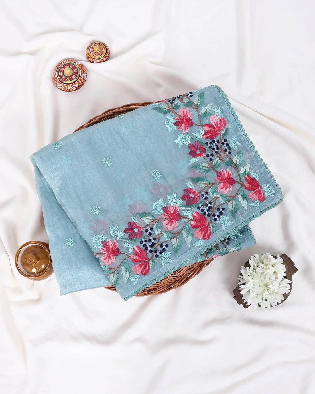 A light blue-green saree with pink and green floral embroidery along the border