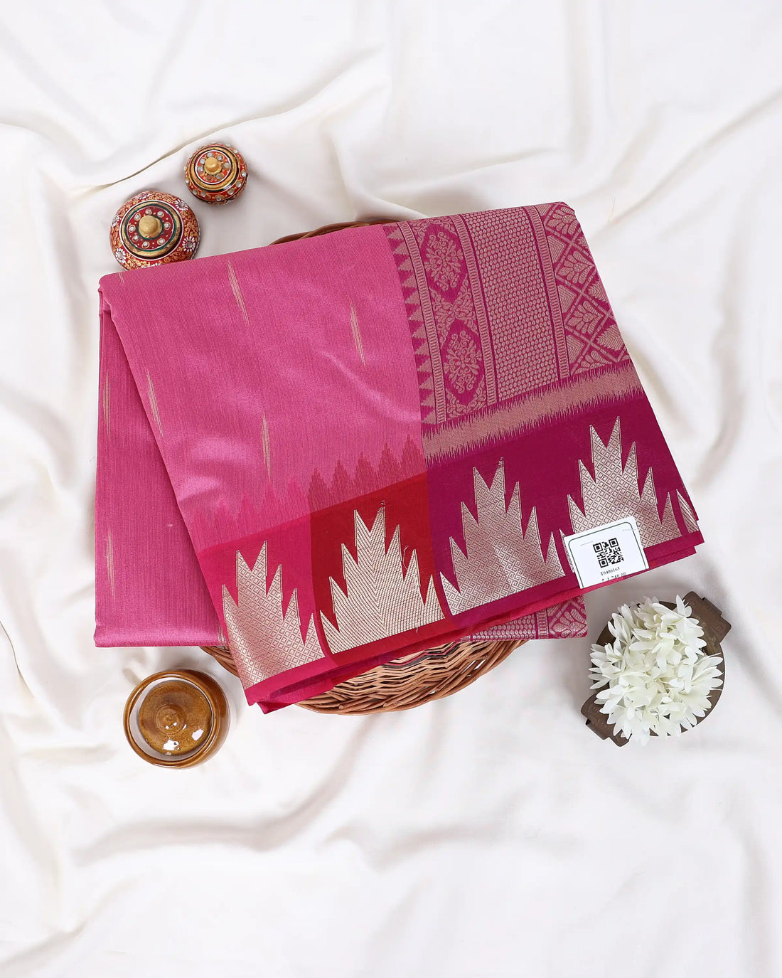 A pink silk saree with a metallic gold and beige geometric border