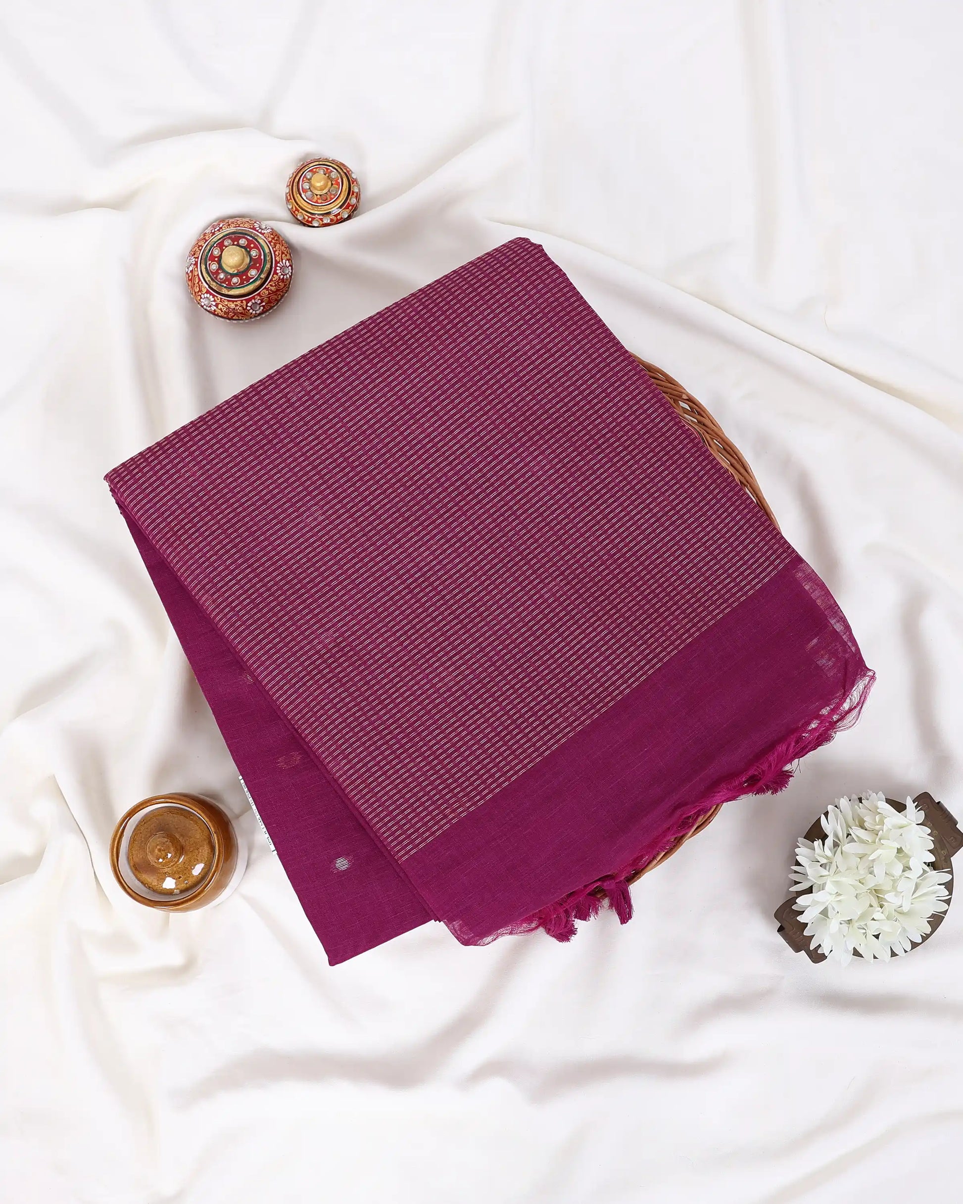 A folded deep magenta-purple saree with a subtle woven texture and a sheer border