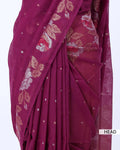 A close-up of a draped magenta-purple saree with woven floral motifs in beige, pink, and white, featuring small metallic dot embellishments.