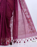 A close-up of a draped saree in deep magenta with a sheer pink pallu featuring floral embroidery and tassel borders