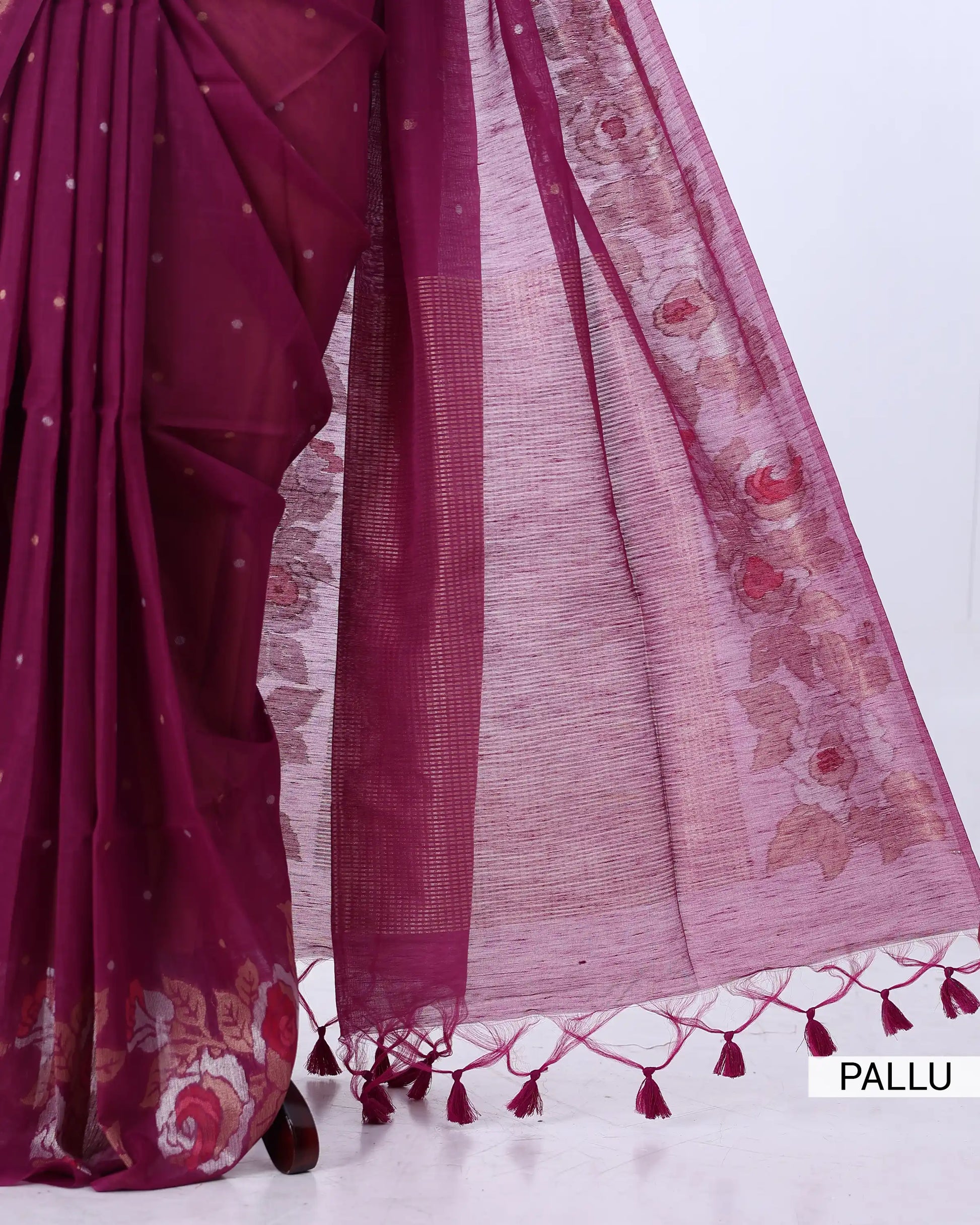 A close-up of a draped saree in deep magenta with a sheer pink pallu featuring floral embroidery and tassel borders