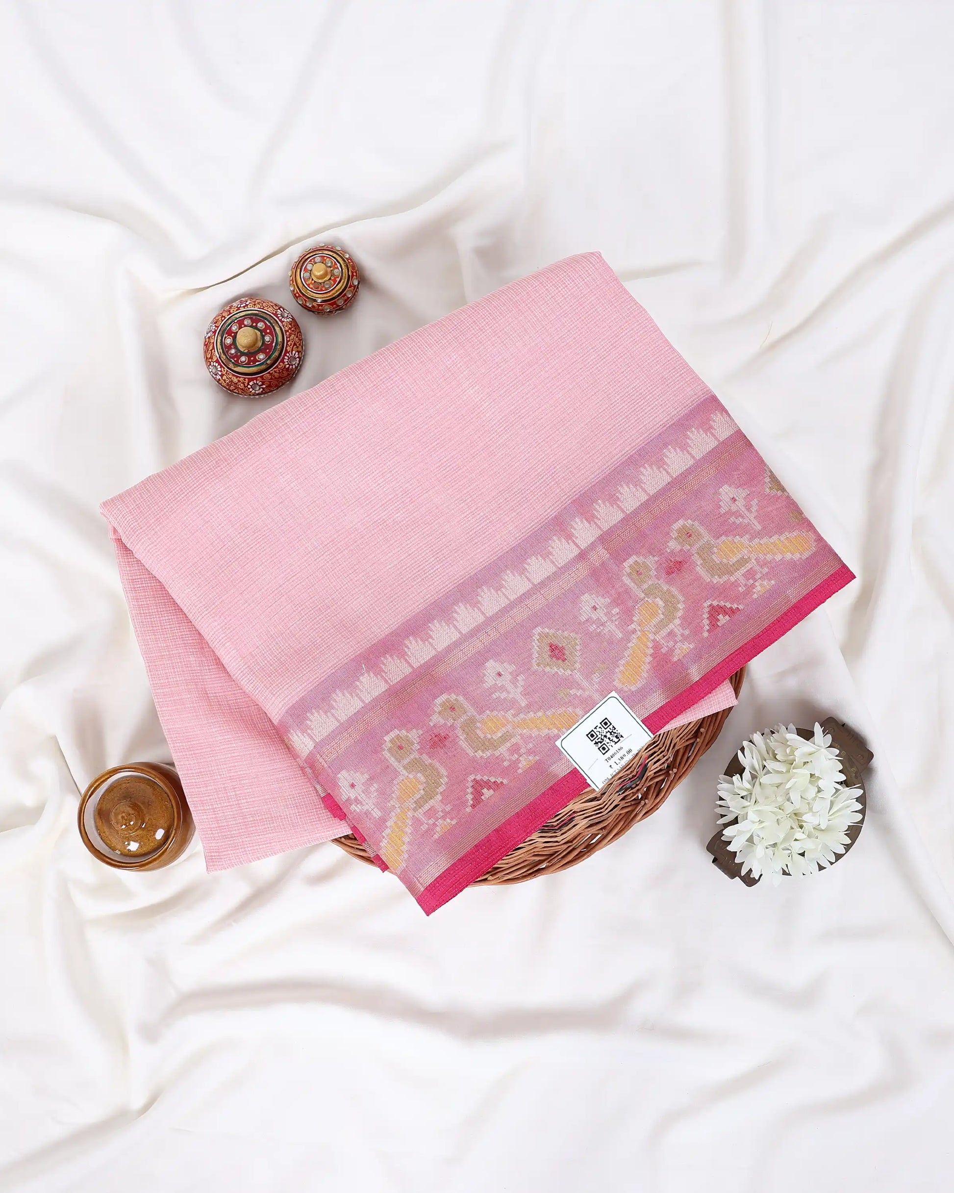 A folded pink saree with a detailed floral and geometric border pattern in shades of pink, yellow, and red