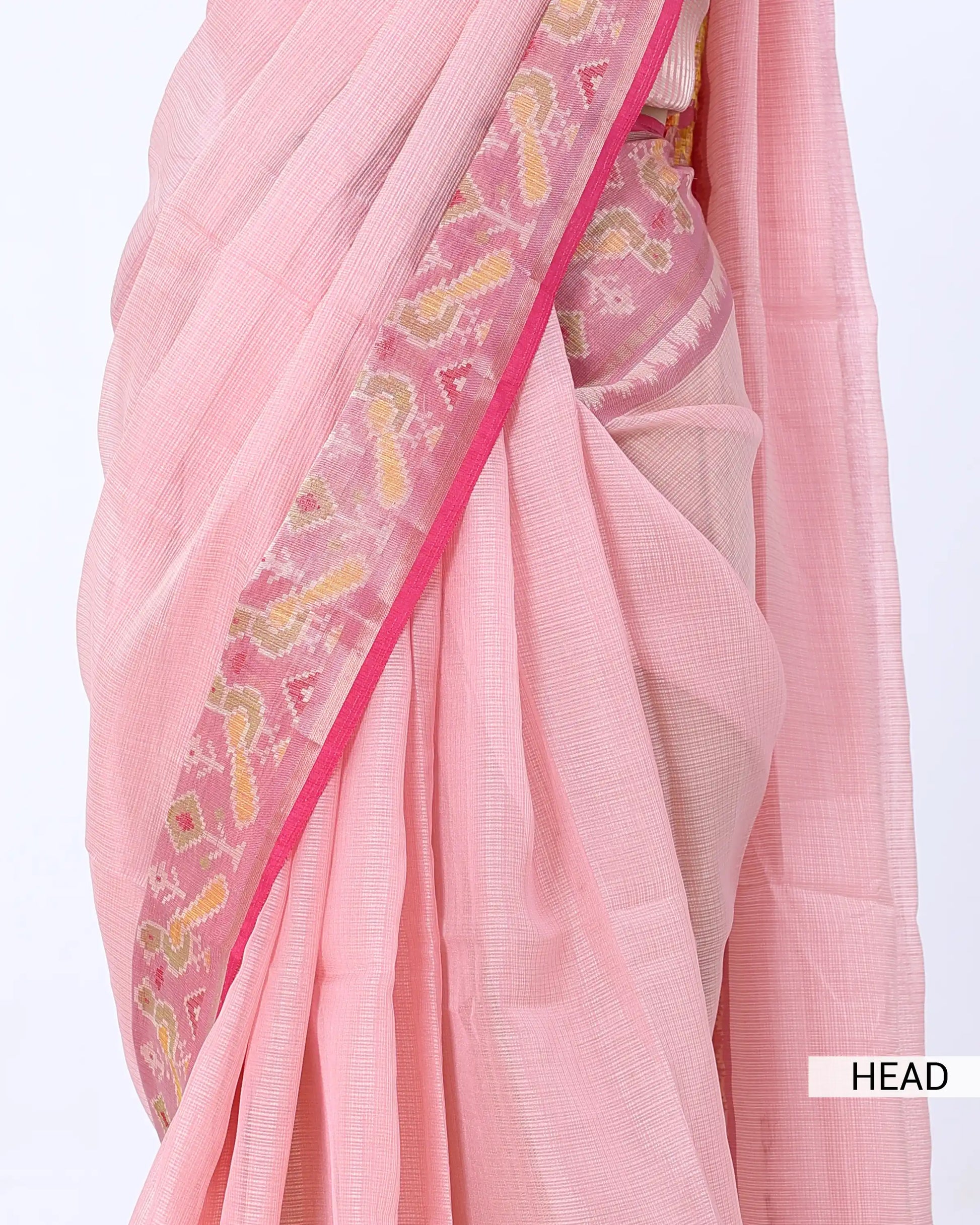 A close-up of a light pink saree with a wide decorative border featuring pink, yellow, and white floral patterns, draped elegantly