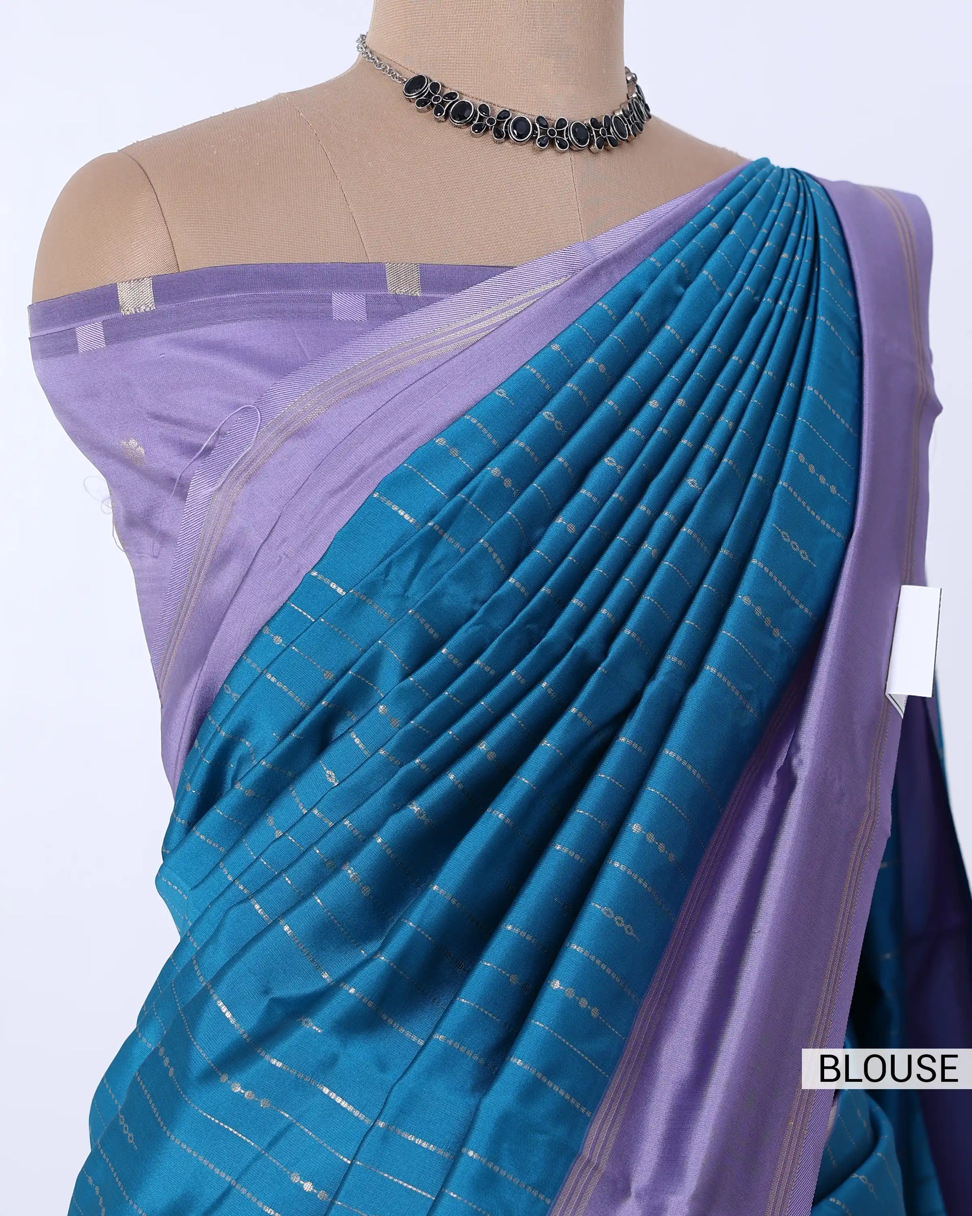 A blue and purple saree  featuring a pleated blue body with thin metallic stripes, a lavender purple border, and a matching lavender blouse. 