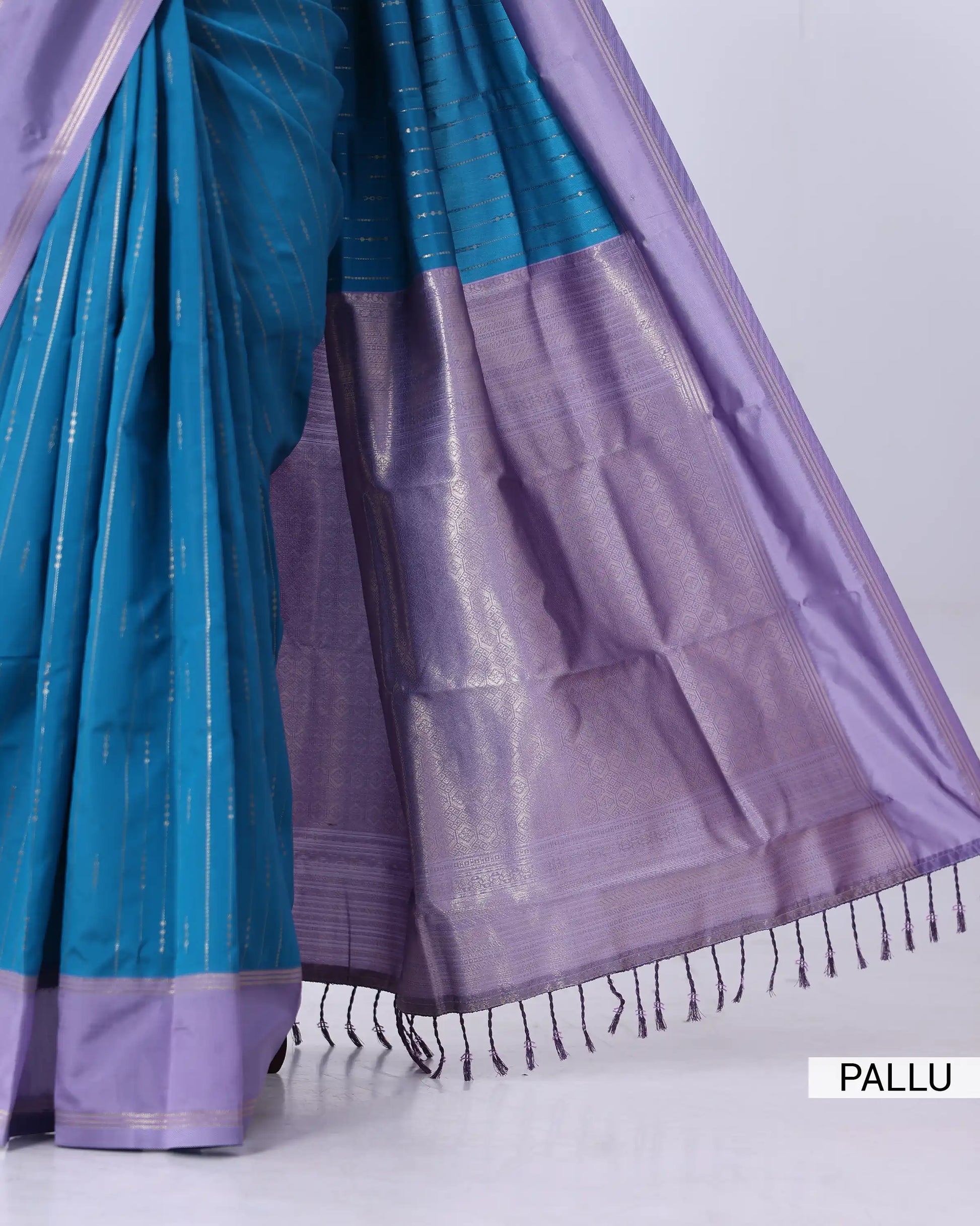 A close-up of a purple and teal silk saree with metallic zari detailing, draped to show the pallu and border