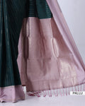 A close-up of a silk saree with a dark green body featuring fine vertical stripes and a wide, shimmering light pink pallu border with tassels.
