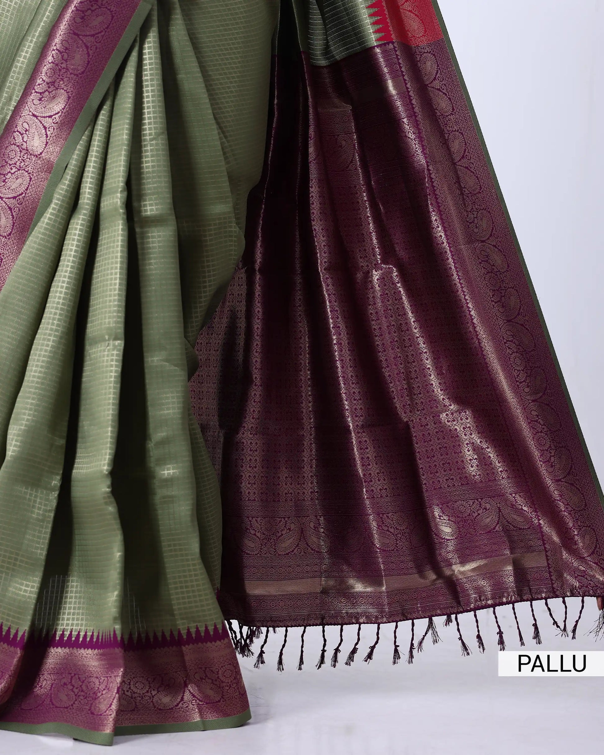 A close-up of a traditional Indian saree with a sage green body, deep purple borders, and metallic gold zari work