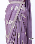 A close-up of a draped purple saree with white floral motifs and a decorative border