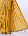 A close-up of a draped yellow saree or fabric with metallic gold floral embroidery and a scalloped gold border