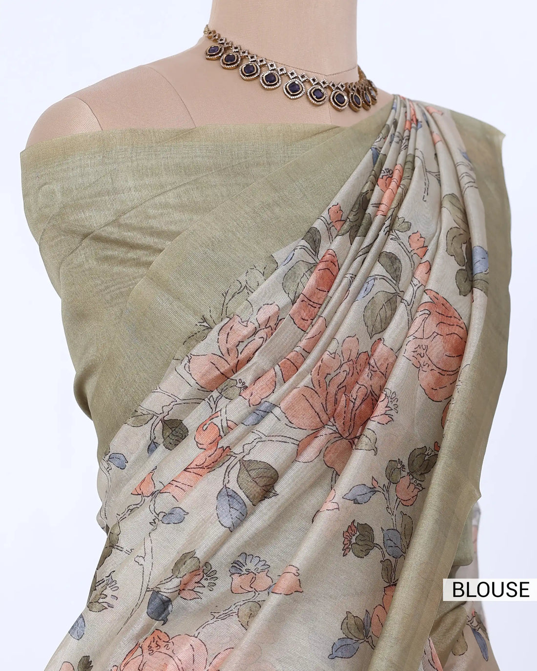 A traditional Indian saree  features a light sage green blouse and a semi-sheer drape with a beige base and a delicate floral pattern in muted pink, orange, and green tones.