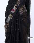A close-up of a black saree with a sheer border featuring beige, red, and white floral embroidery
