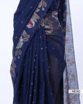 A close-up of a navy blue saree with floral and paisley patterns in beige, red, and white, featuring small metallic dot embellishments