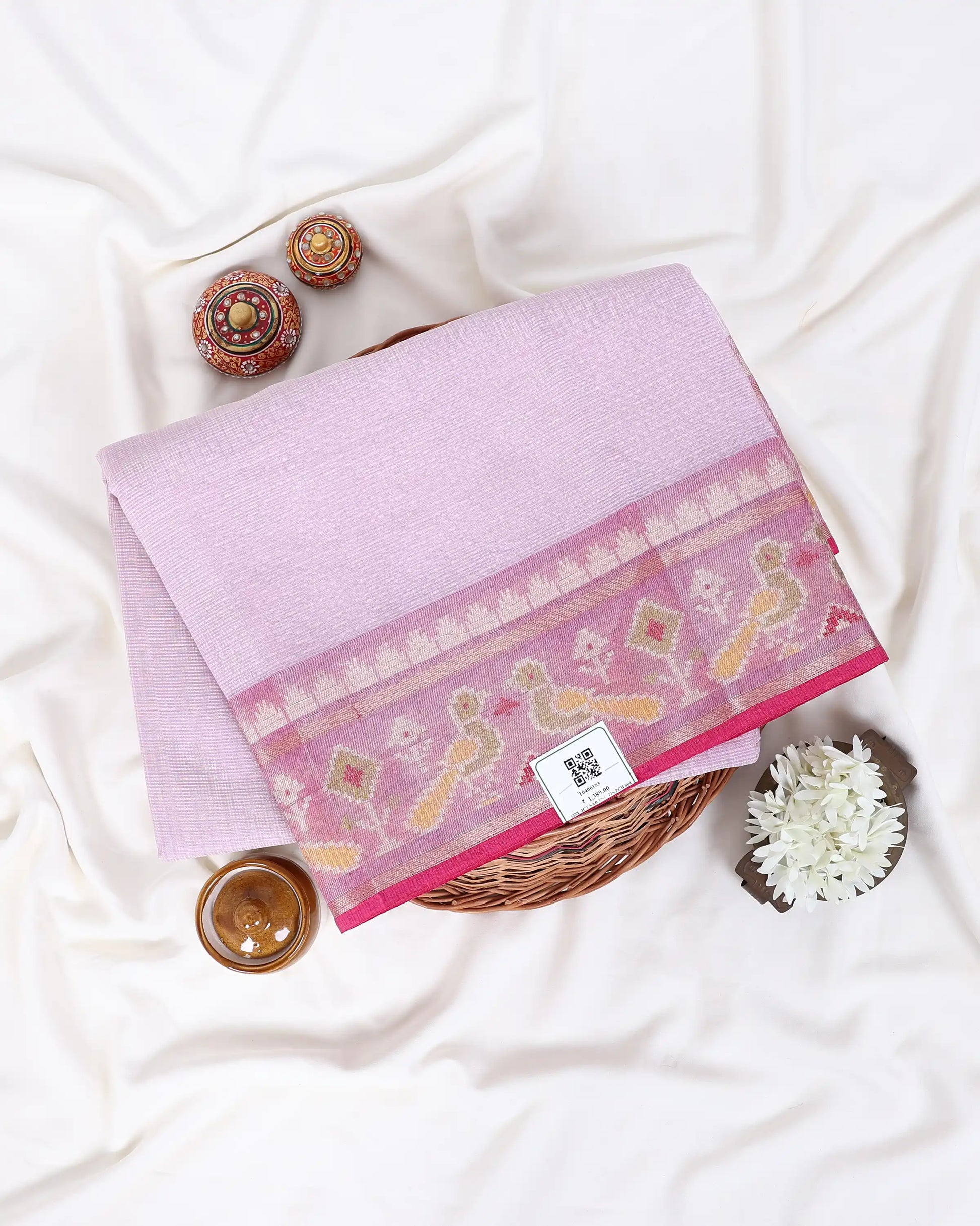 A folded light pink saree with a wide pink border featuring yellow and white floral motifs