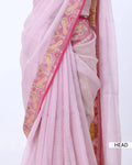 A close-up of a light pink saree with a wide pink border featuring yellow and gold paisley patterns