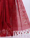 A close-up of a red saree with a matching pallu, showing floral printed detailing, sheer texture, and red tassels along the edge