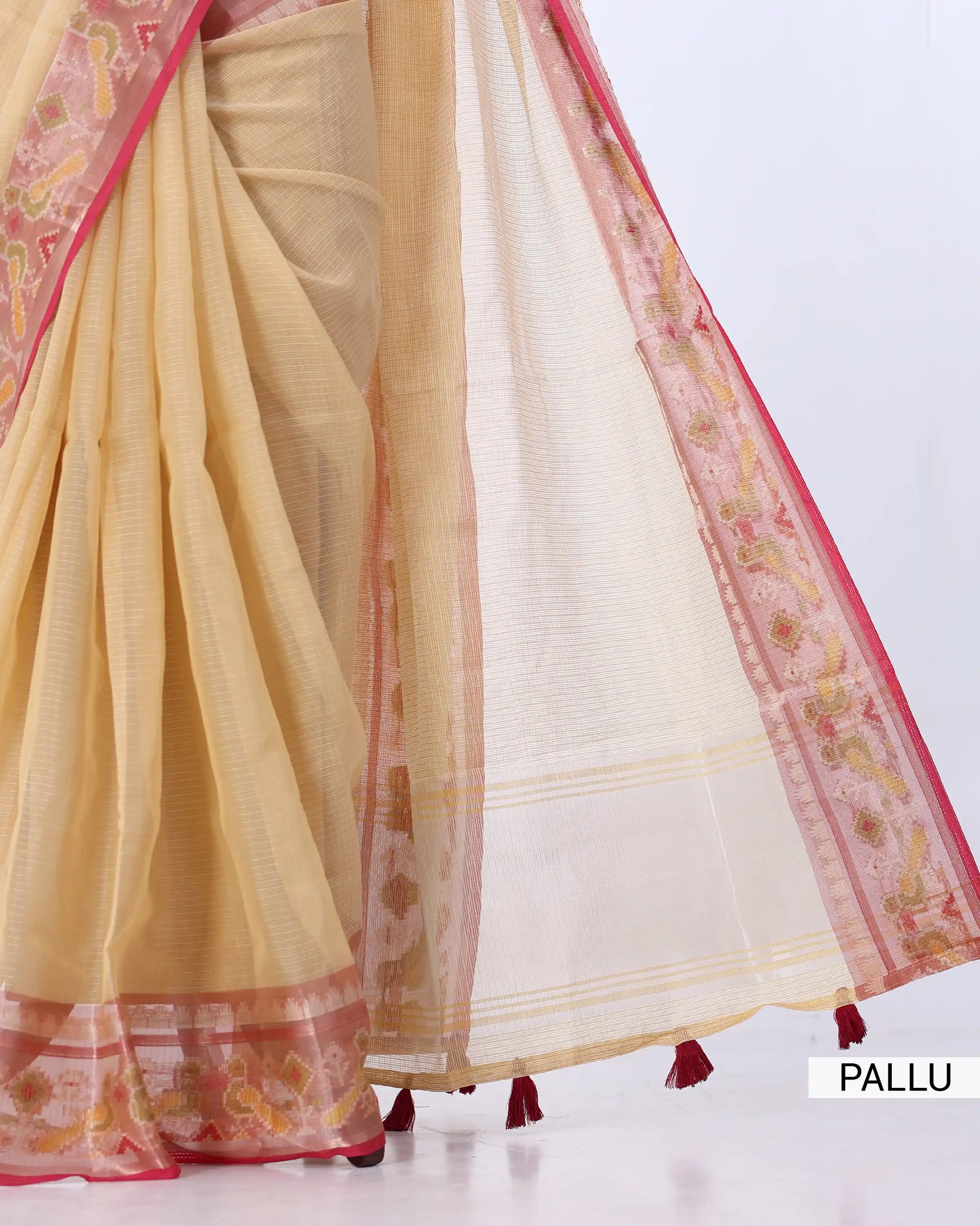 A close-up of a draped saree with a light beige body, a white pallu with pink floral border, and red tassels