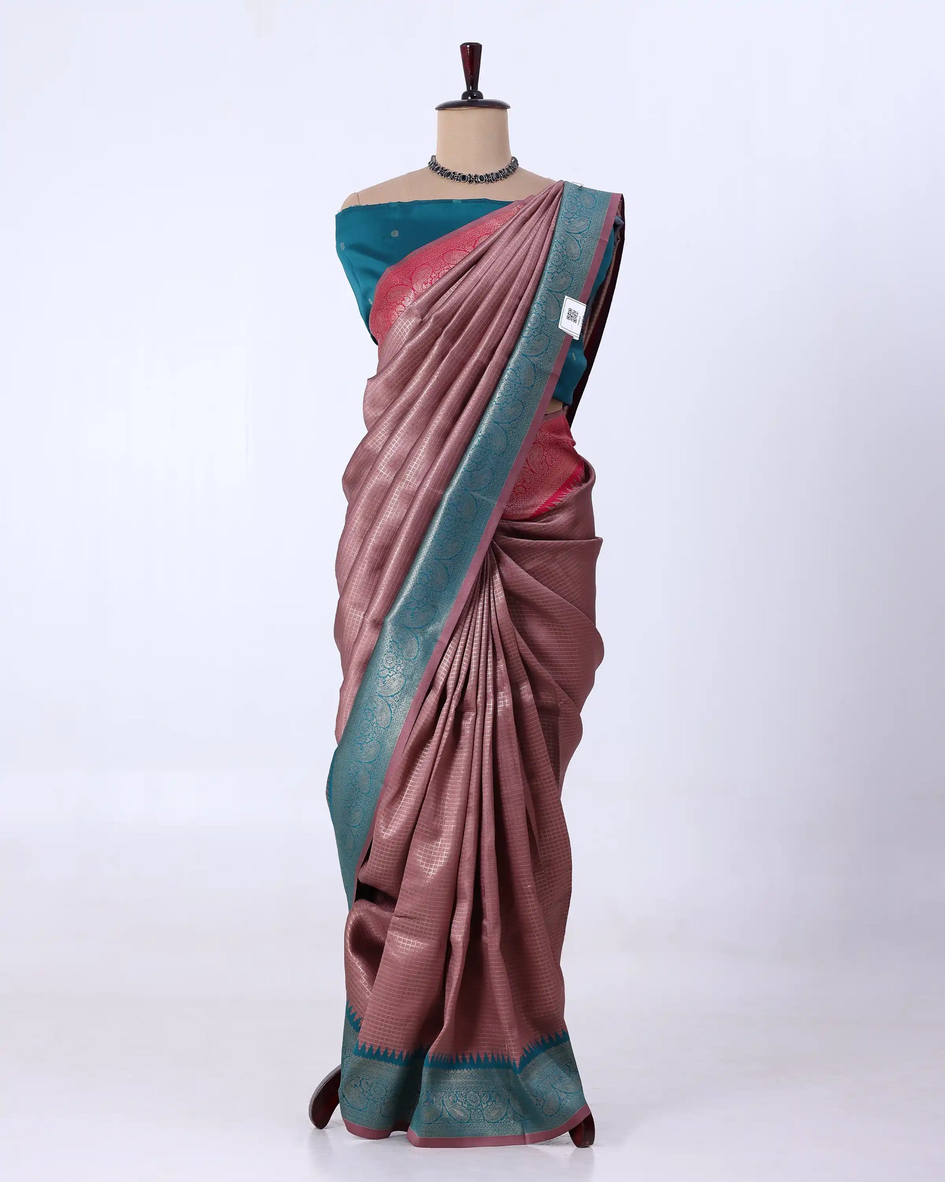 A draped sari has a dusty rose-pink body with a teal-blue border and a matching teal blouse, plus subtle metallic woven detailing.