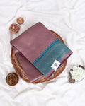A folded silk saree in a dusty mauve color with a teal border