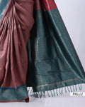 A close-up of a draped saree with a dusty rose body and a dark teal-green border featuring metallic gold zari motifs and tassels