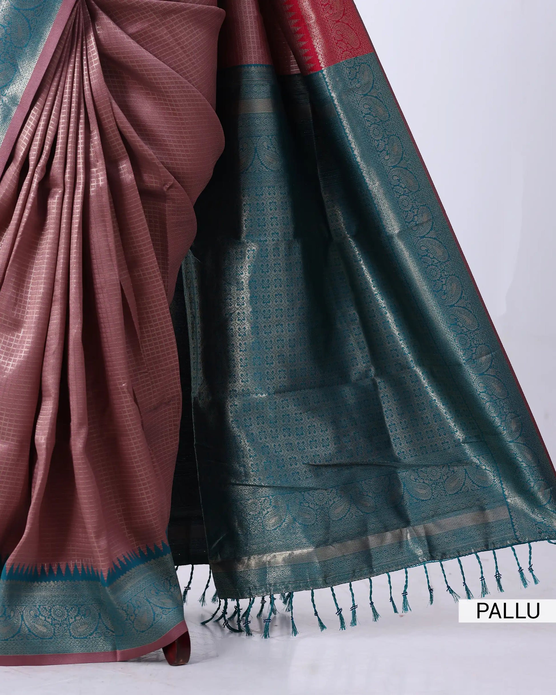 A close-up of a draped saree with a dusty rose body and a dark teal-green border featuring metallic gold zari motifs and tassels
