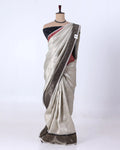 A light beige silk saree with a metallic bronze border and a black blouse
