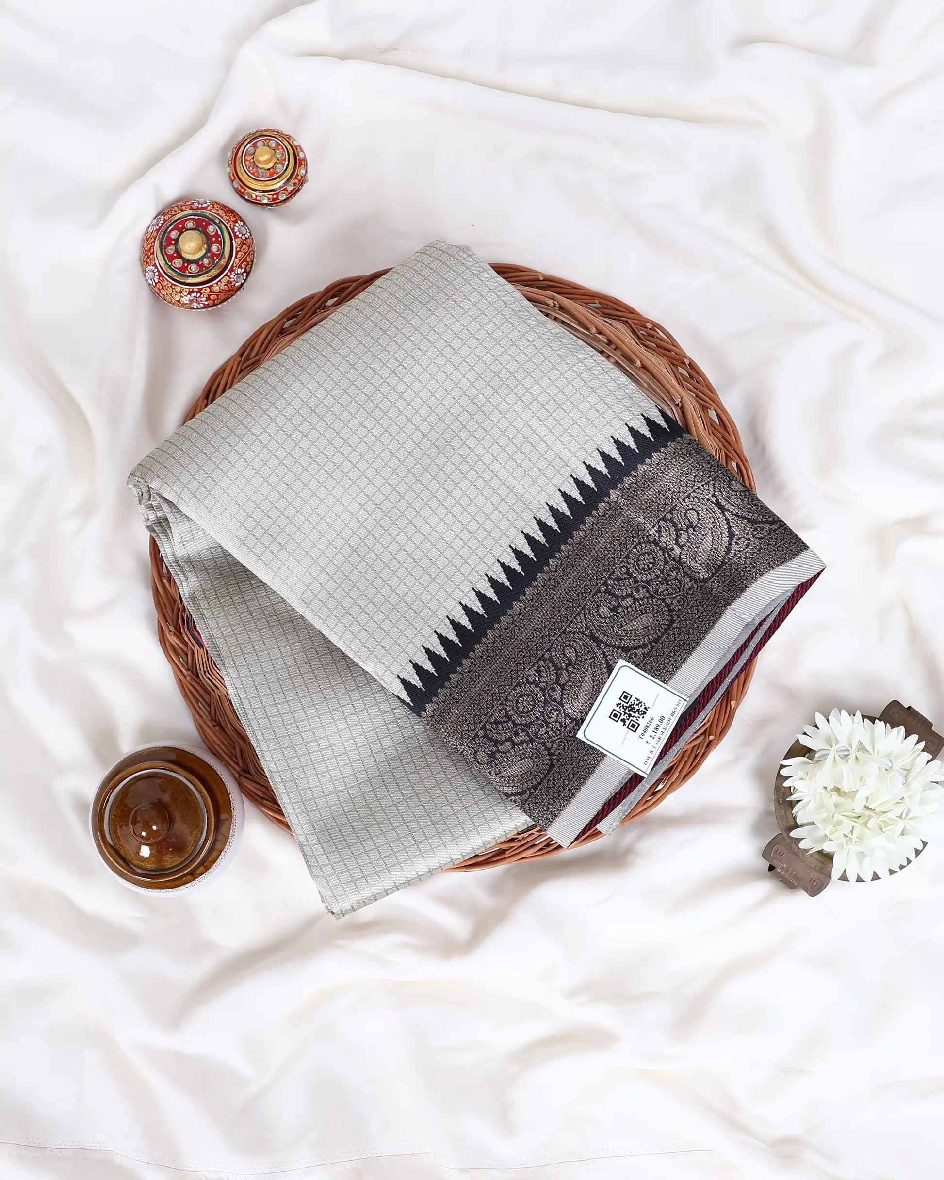 A folded light gray and white checkered saree with a dark gray border and black pointed pattern