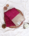A folded magenta and beige silk saree with small gold motifs, displayed on a woven tray 